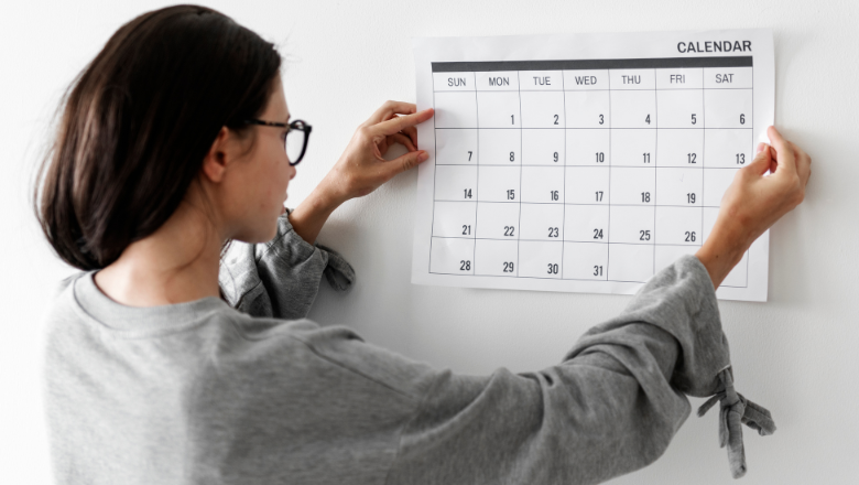 Frau hängt einen Wandkalender auf – symbolisiert die zeitliche Struktur und Planung eines Geschäftsjahrs im Unternehmen.