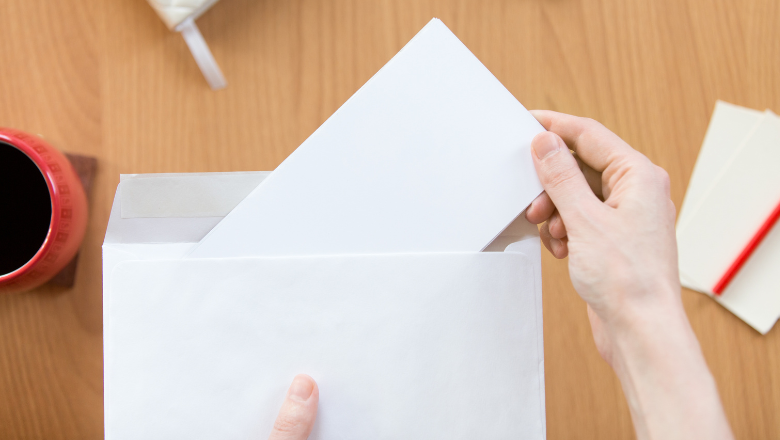 Hand steckt ein Dokument in einen Briefumschlag – stellvertretend für die Kommunikation mit dem Finanzamt zur Steuernummer und Steuer-ID.